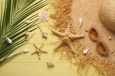 Şık şapkalı, güneş gözlüklü, deniz yıldızlı, deniz kabuklu ve ahşap arka planda palmiye yapraklı kompozisyon