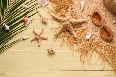 Şık şapkalı, güneş gözlüklü, deniz yıldızlı, deniz kabuklu ve ahşap arka planda palmiye yapraklı kompozisyon