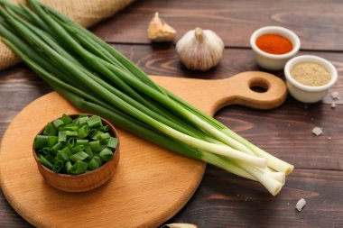 Board with fresh green onion on wooden background