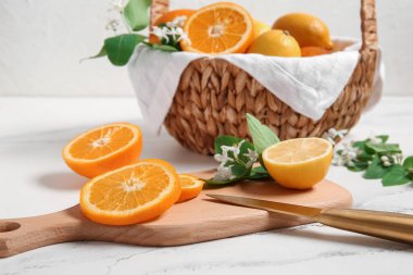 Bir sepet portakal ve beyaz masa üzerinde açan dalları olan limonlar.