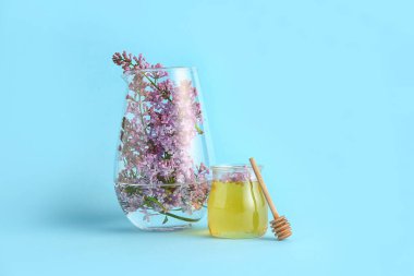 Cam vazoda leylak dalı ve mavi arka planda bal kavanozu