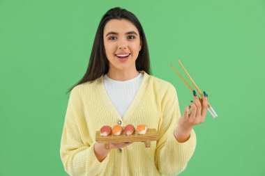 Yeşil arka planda suşi ve çubuklarla mutlu genç bir kadın.