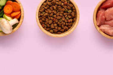 İçinde kuru hayvan mamaları, çiğ et ve pembe arka planda doğal ürünler olan kaseler.