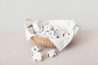 Pamuk çiçekleri sepetin içinde, duvarın yanındaki gri masada havlu var.