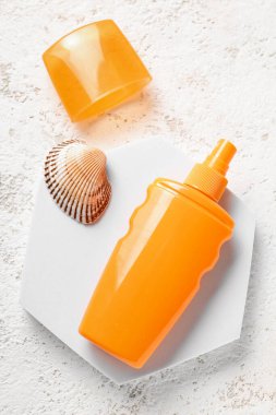 Güneş kremi şişesi ve beyaz arka planda deniz kabuklarıyla dur.