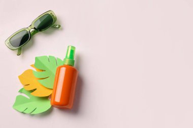 Kağıt palmiye yaprakları ve beyaz arka planda güneş gözlüğü olan bir şişe güneş kremi.