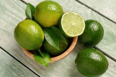 Yeşil ahşap arka planda taze limon ve yapraklı kase.