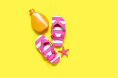 Deniz yıldızlı bir şişe güneş kremi ve sarı arka planda parmak arası terlik.