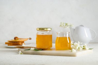 Arkaplanda akasya çiçekleri olan bal kavanozları