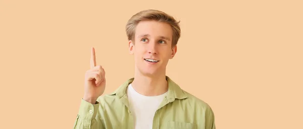 Junger Mann Mit Zahnspange Und Erhobenem Zeigefinger Auf Beigem Hintergrund — Stockfoto