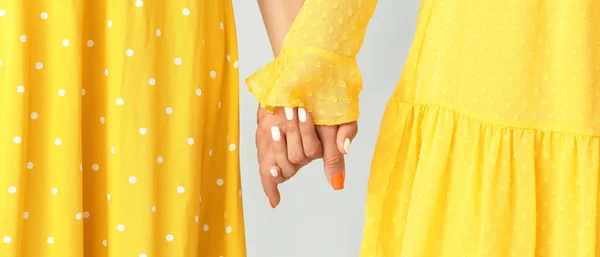 Jovens Mulheres Vestidos Amarelos Mãos Dadas Fundo Cinza Close — Fotografia de Stock