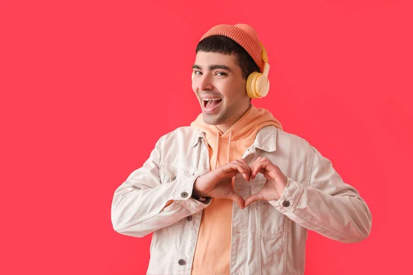 Mladý Muž Sluchátkách Aby Tvar Srdce Rukama Červeném Pozadí — Stock fotografie