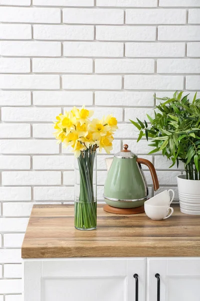 開花ナルシシズムの花と花瓶 電気ケトル キッチンカウンターのカップと観葉植物 — ストック写真