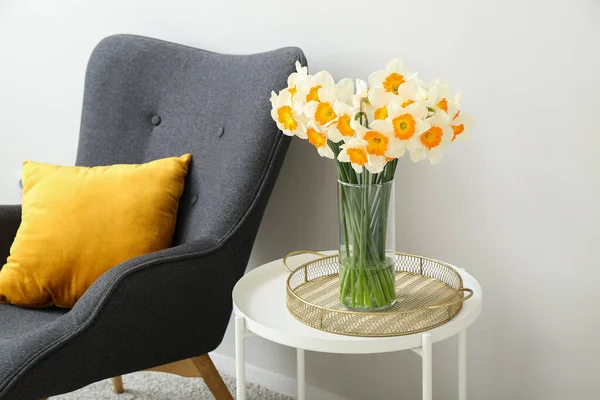 白い壁の近くのコーヒーテーブルの上に咲くナルシスの花と居心地の良い灰色のアームチェアと花瓶 — ストック写真