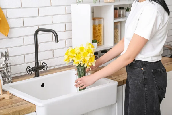 Woman taking vase with narcissus flowers from sink in kitchen