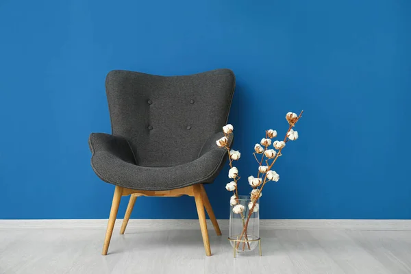 Stock image Vase of cotton sprigs and armchair near blue wall