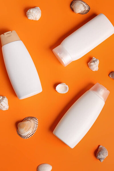 Bottles of sunscreen cream with seashells on orange background