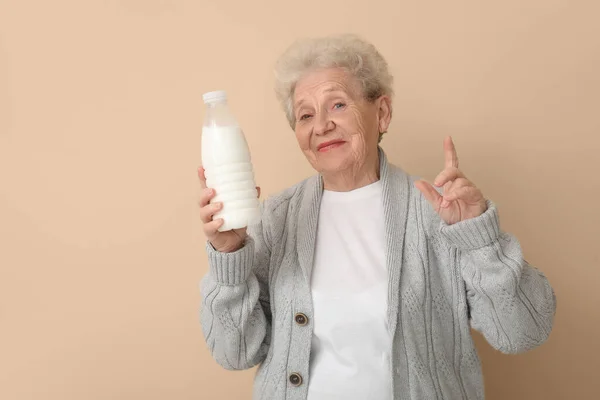Seniorin Mit Milchflasche Zeigt Auf Etwas Auf Beigem Hintergrund — Stockfoto