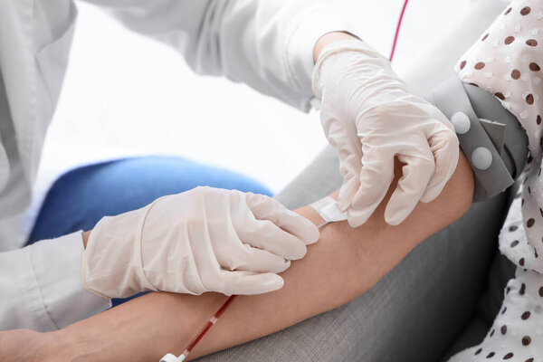 Female doctor taking young donor's blood in clinic, closeup