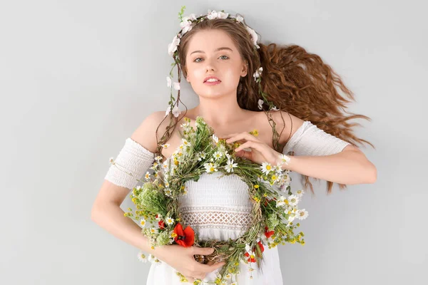 光の背景に花の花輪を持つ美しい若い女性 — ストック写真