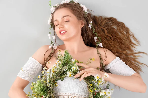 光の背景に花の花輪を持つ美しい若い女性 — ストック写真