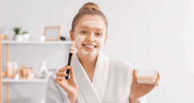 Zerdeçal maskeli ve banyoda fırçası olan güzel genç bir kadın.