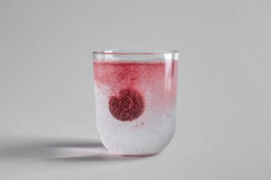 Gri zemin üzerinde çözünebilir tablet bulunan bir bardak su.