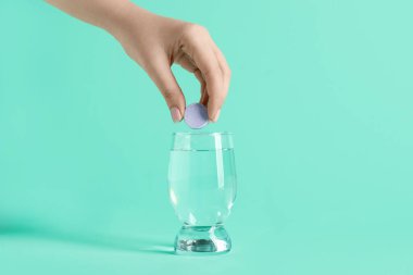 Kadın eli, çözünür masayı turkuaz arka planda su bardağına koyuyor.