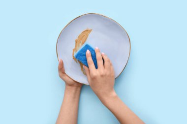 Kadın elleri kirli tabakları süngerle yıkıyor mavi arka planda