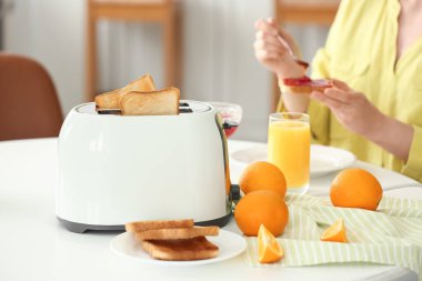 Günümüz tost makinesi, portakal ve kızarmış ekmek dilimleriyle sofrada kahvaltı eden bir kadın.