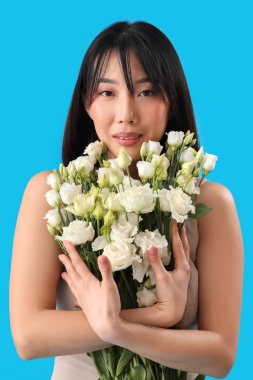 Güzel Asyalı kadın mavi arka planda bir buket Eustoma çiçeği tutuyor.
