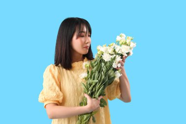 Güzel Asyalı kadın mavi arka planda bir buket Eustoma çiçeği tutuyor.