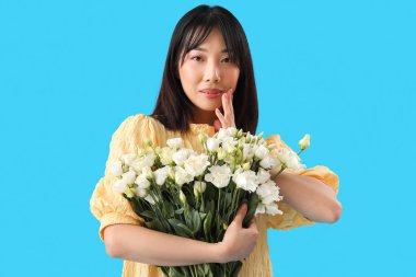 Güzel Asyalı kadın mavi arka planda bir buket Eustoma çiçeği tutuyor.
