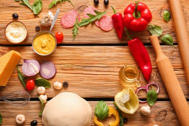 Çiğ hamurdan yapılmış çerçeve ve ahşap arka planda pizza hazırlamak için malzemeler