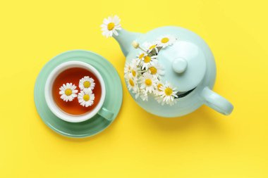 Bir fincan doğal papatya çayı ve sarı arka planda çiçekler.
