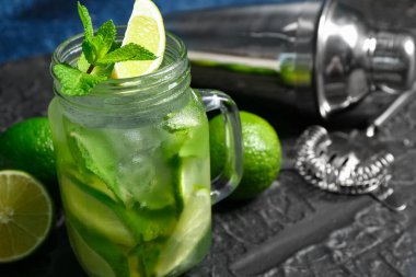 Mason kavanozu soğuk mojito ve siyah masada limon karıştırıcı.