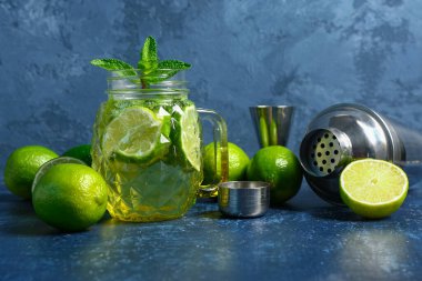 Mason kavanozu soğuk mojito ve mavi masada limon karıştırıcı.
