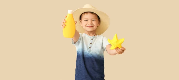 日焼け止めクリームとベージュの背景にヒトデを持つ小さな男の子 — ストック写真