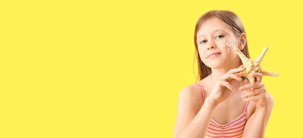 Little girl with sunscreen cream on her face and starfish on yellow background with space for text