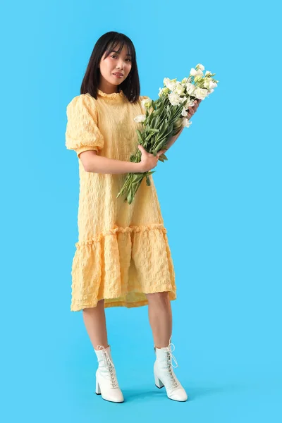 美しいアジアの女性が青い背景に花の花束を持っています — ストック写真