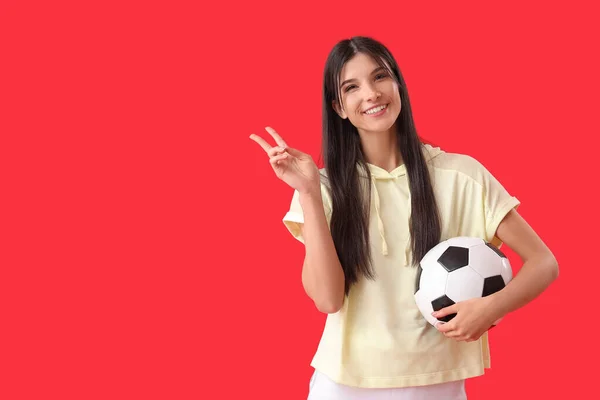 Mladá Žena Fotbalový Míč Ukazuje Vítězství Gesto Červeném Pozadí — Stock fotografie