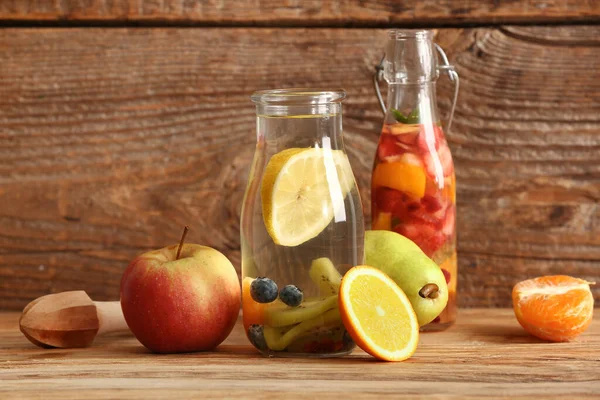 stock image Bottles of infused water with different sliced fruits on wooden table