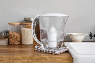 Su filtresi sürahisi mutfak tezgahında, ışık duvarının yanında.