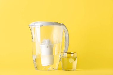 Sarı arka planda su filtresi sürahi ve cam.