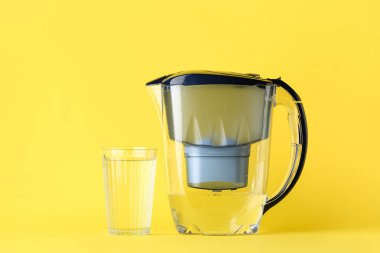 Sarı arka planda su filtresi sürahi ve cam.