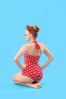 Young pin-up woman in polka dot swimsuit on blue background