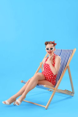 Mavi arka planda, güverte koltuğunda oturan genç kadın.