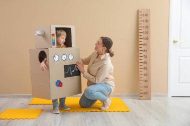 Evde dadısı olan kartondan robot kostümlü küçük çocuk.