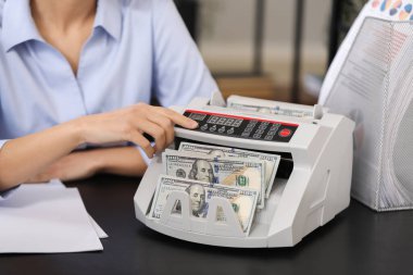 Kadın banka müdürü ofiste para sayma makinesi kullanıyor, yakın plan.