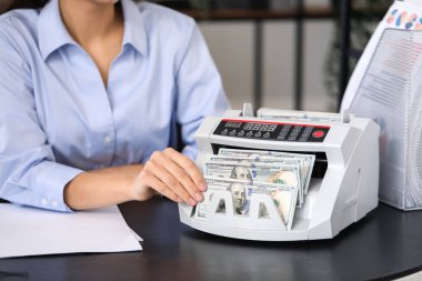Kadın banka müdürü ofiste para sayma makinesi kullanıyor, yakın plan.